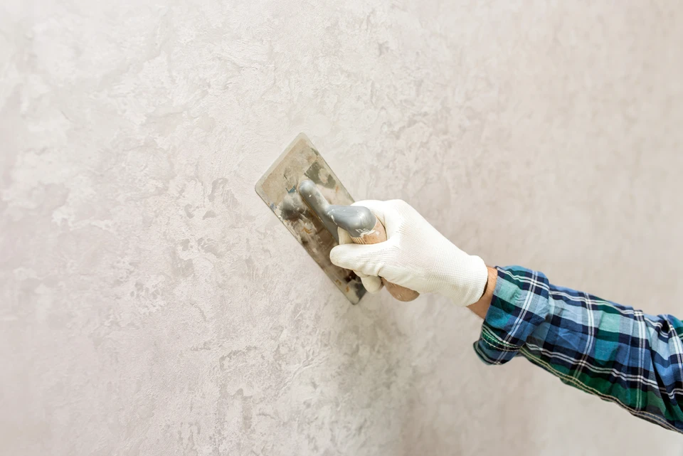 Femme souriante dans atelier de poterie faisant un cœur avec ses mains, portant tablier et pull gris clair