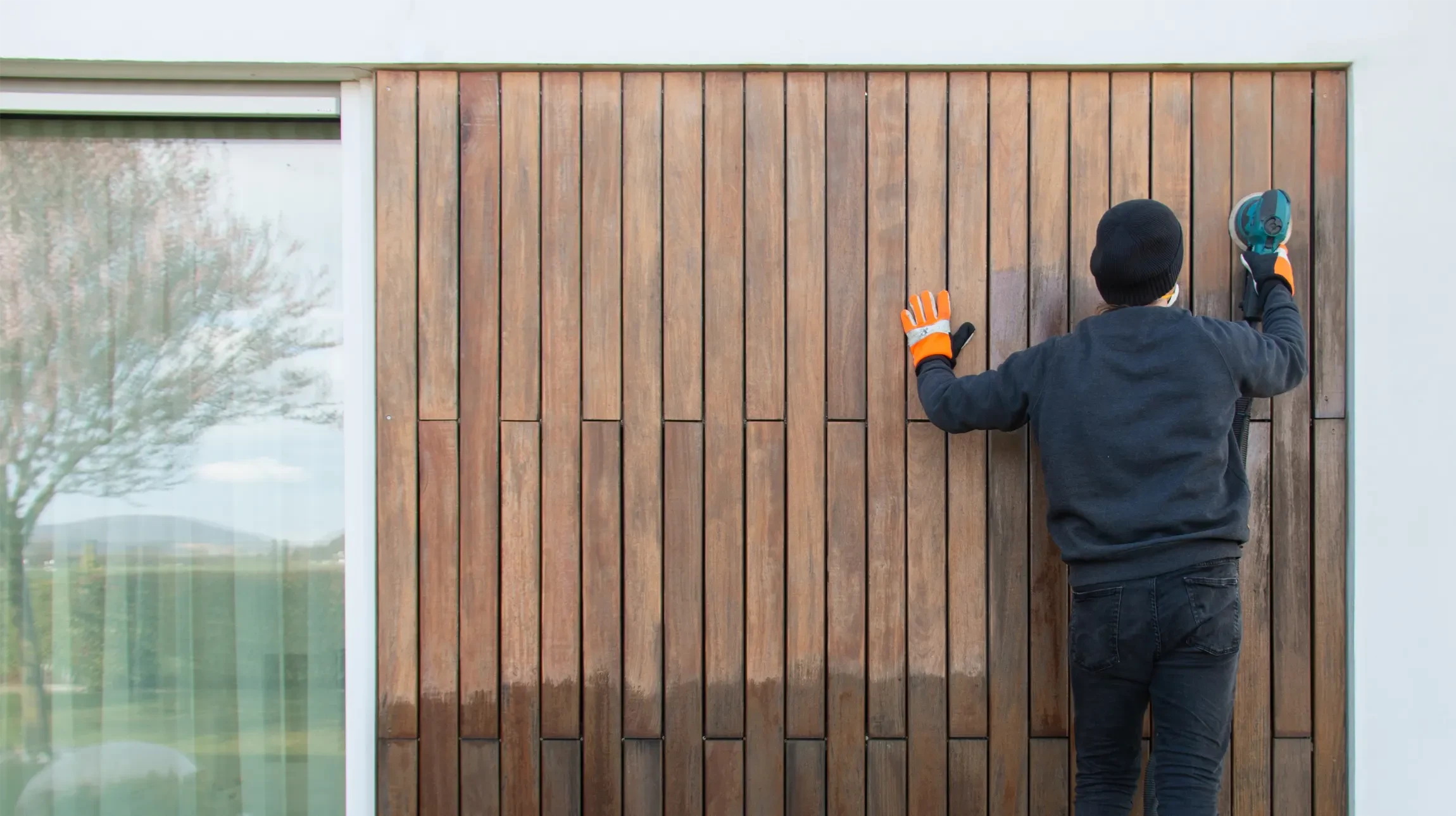Entrée extérieure d'une maison avec mur blanc en briques peintes, porte d'entrée grise à panneaux avec vitrage texturé et poignée chromée