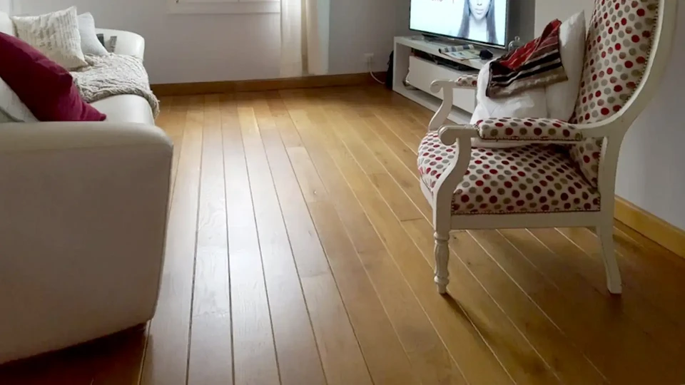 Salon lumineux avec canapé Chesterfield blanc, lampadaire trépied à abat-jour gris, grandes baies vitrées donnant sur jardin verdoyant